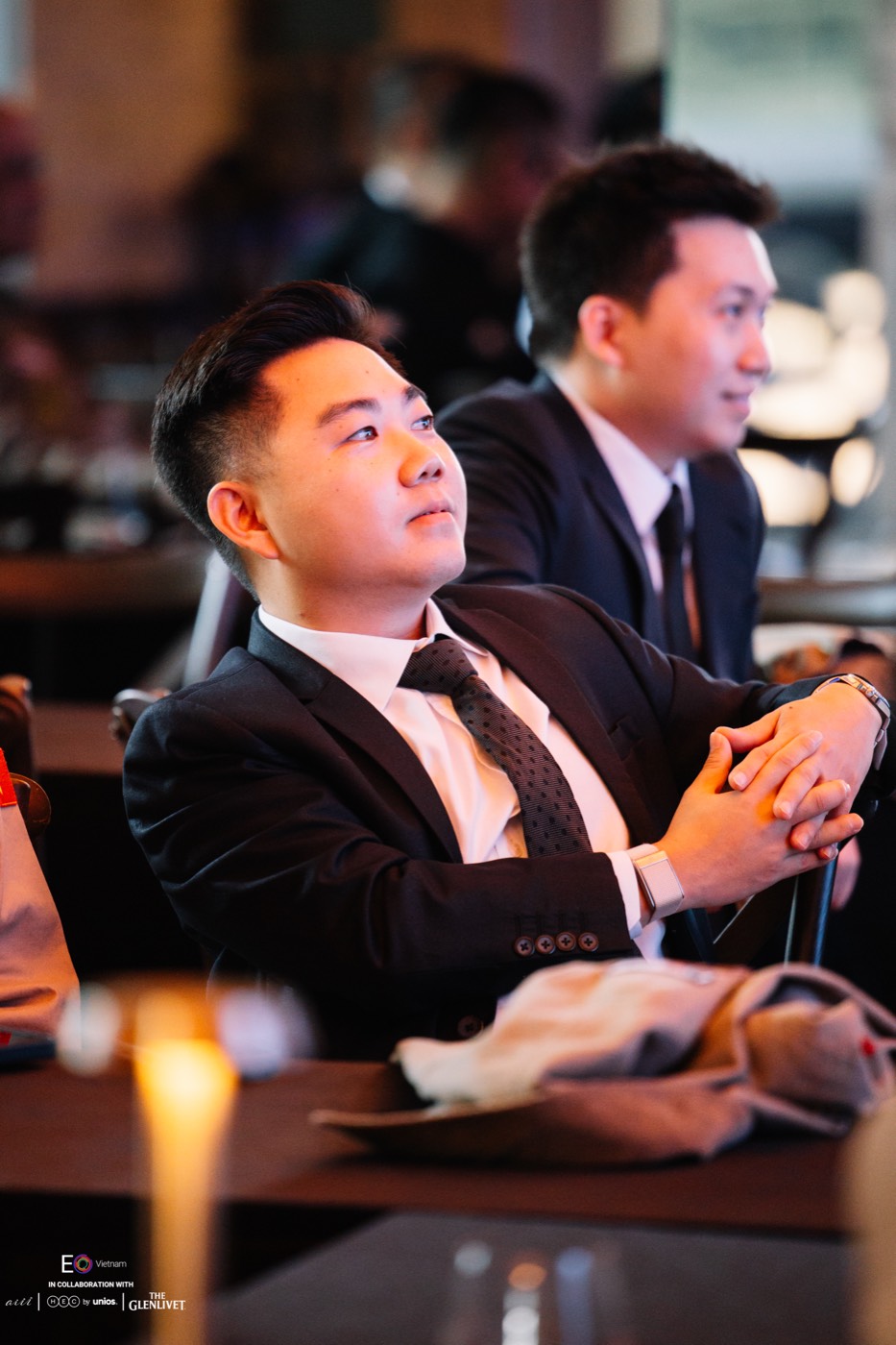 Bryan Loo in a dark suit and patterned tie, looking up at an EO Vietnam event