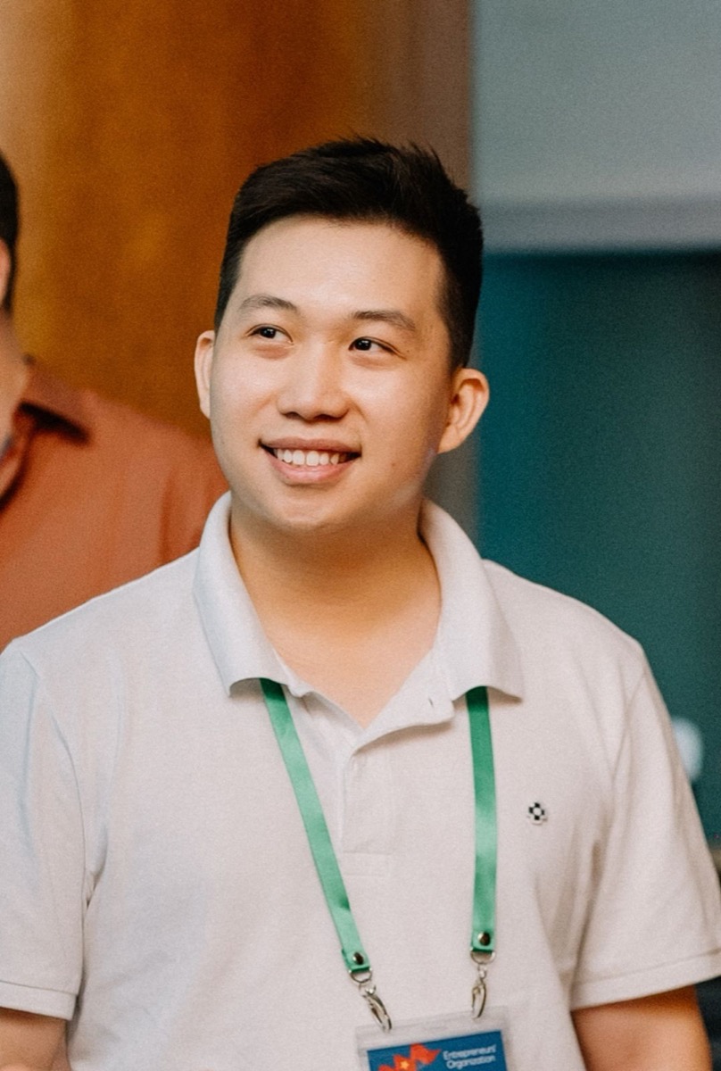 Hoang Le in a white polo with a green EO lanyard, smiling at an EO Vietnam event